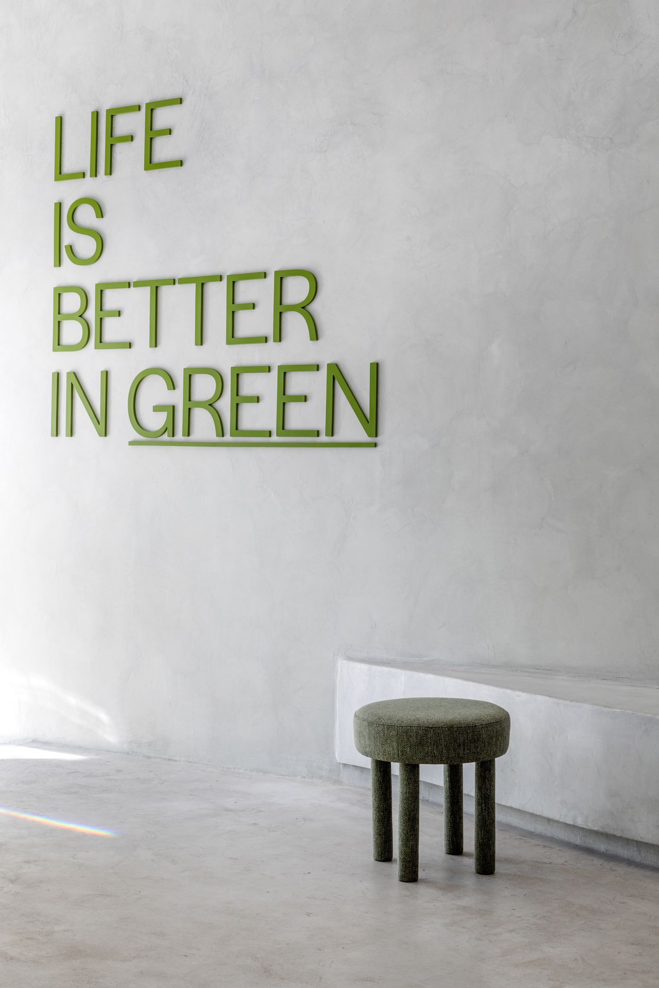 A white-washed, plastered matcha cafe with sculptural decor features monochromatic furnishings and an emerald green and chrome bar counter.