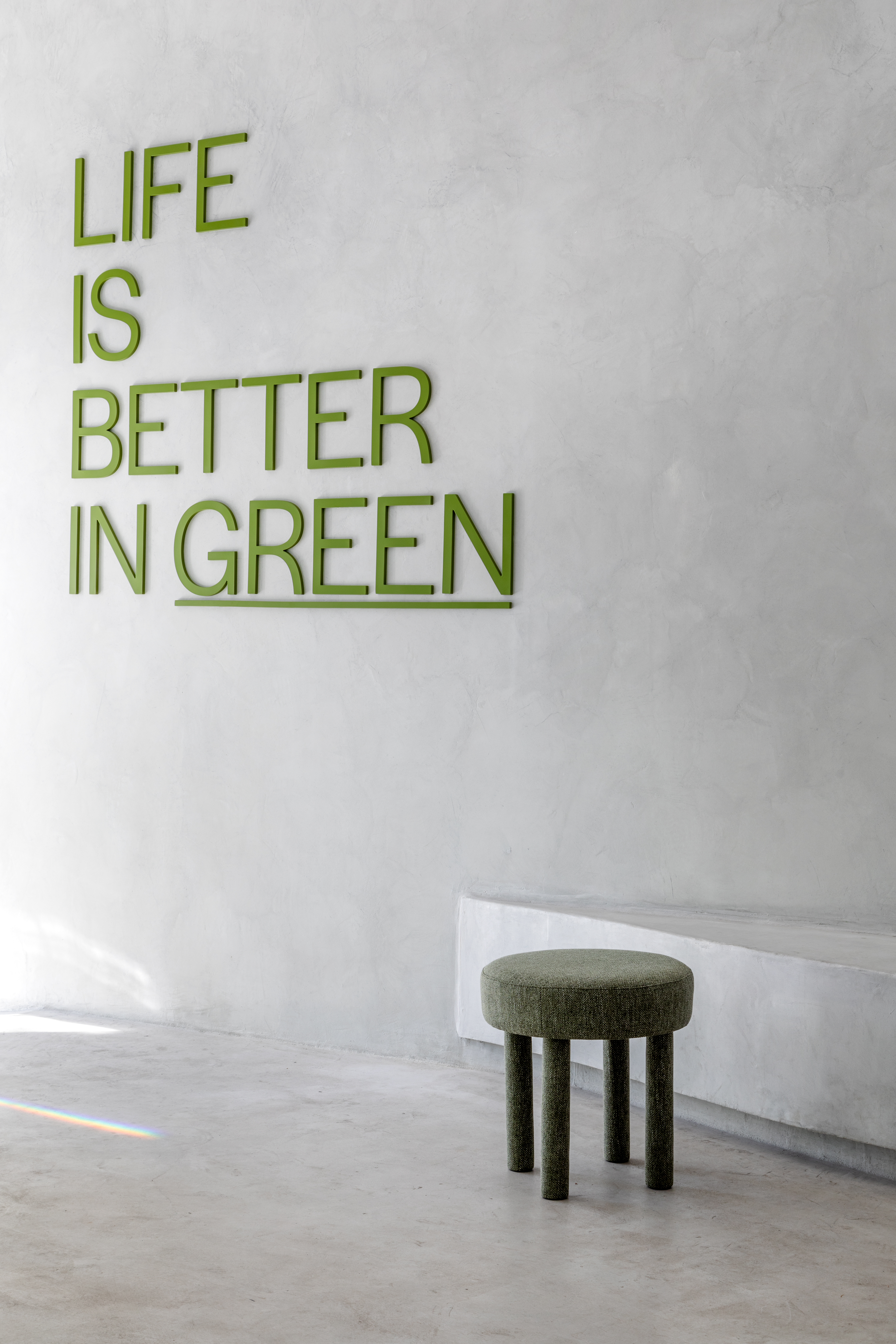 A white-washed, plastered matcha cafe with sculptural decor features monochromatic furnishings and an emerald green and chrome bar counter.