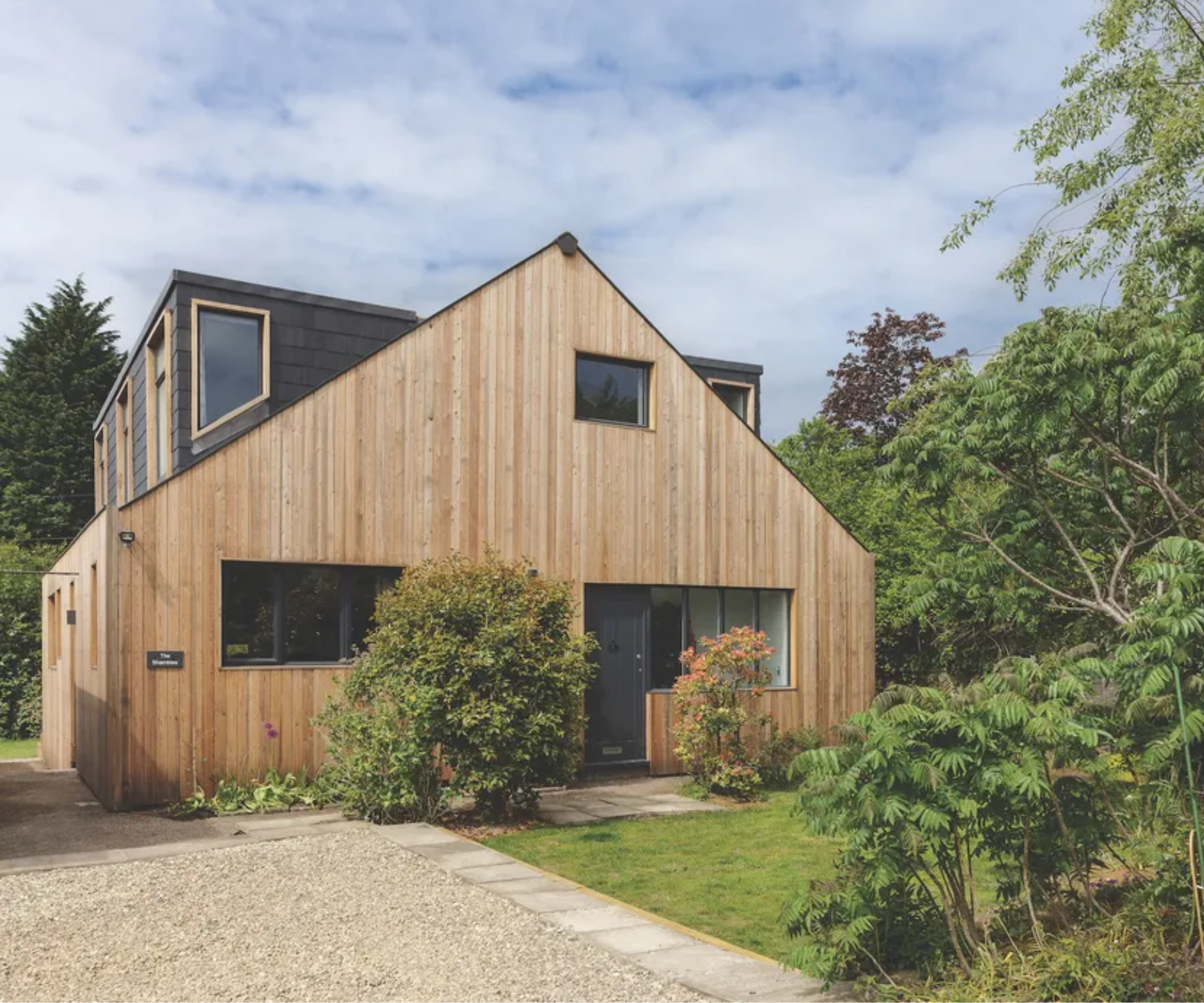 Exterior of wooden cladded house with gravel to the left front and lawn to the right front with a patio strip in between