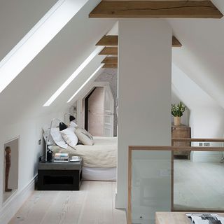 bedroom with white wall bed with white cushions bedside lamps and wooden floor