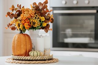 A beautiful autumnal bouquet of orange, yellow, and red flowers displayed in a pumpkin vase.