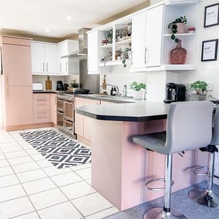 After view of Pink Frenchic painted kitchen cupboards with grey barstools at dark counter tops