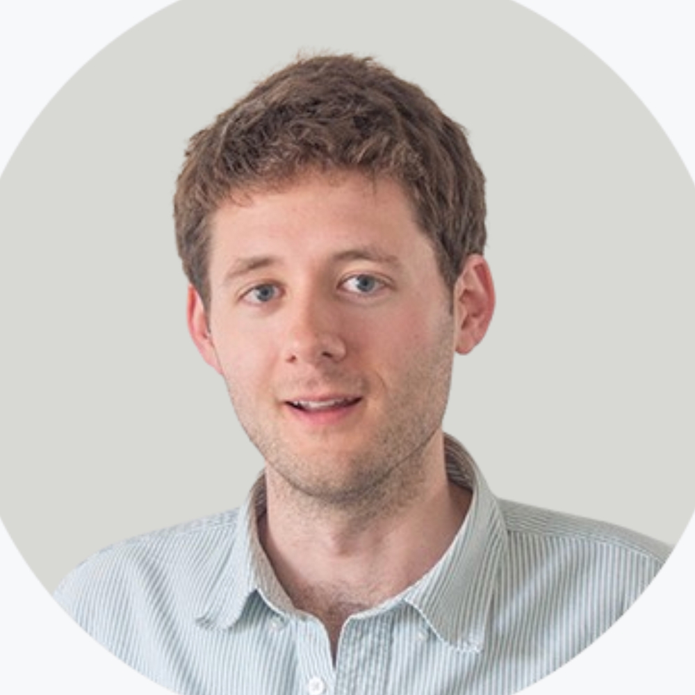Young man with curly brown hair in a striped shirt, circular-cropped headshot on a pale background