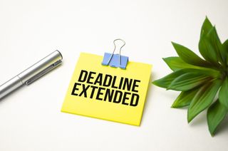 Words DEADLINE EXTENDED on a desk with a pen and plant