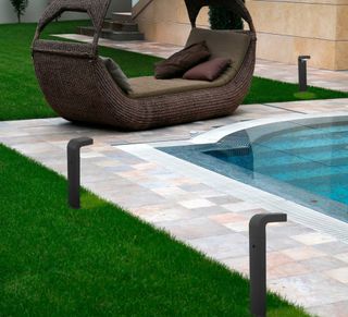 A swimming pool with a patio, low-level exterior lighting and brown seating