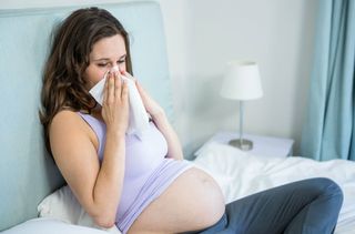 A women sat on a bed suffering from hay fever when pregnant