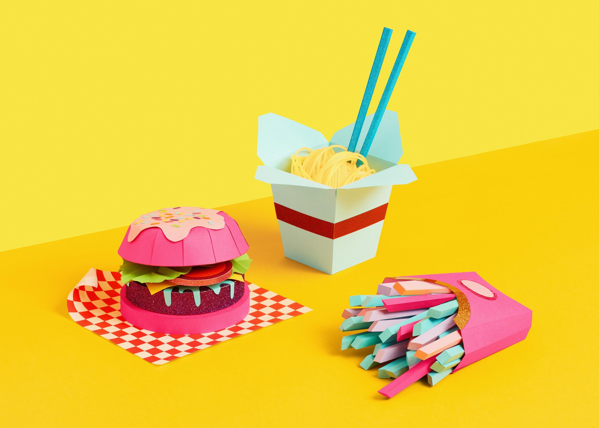  An origami burger, origami noodles and origami fries displayed on a yellow background. 
