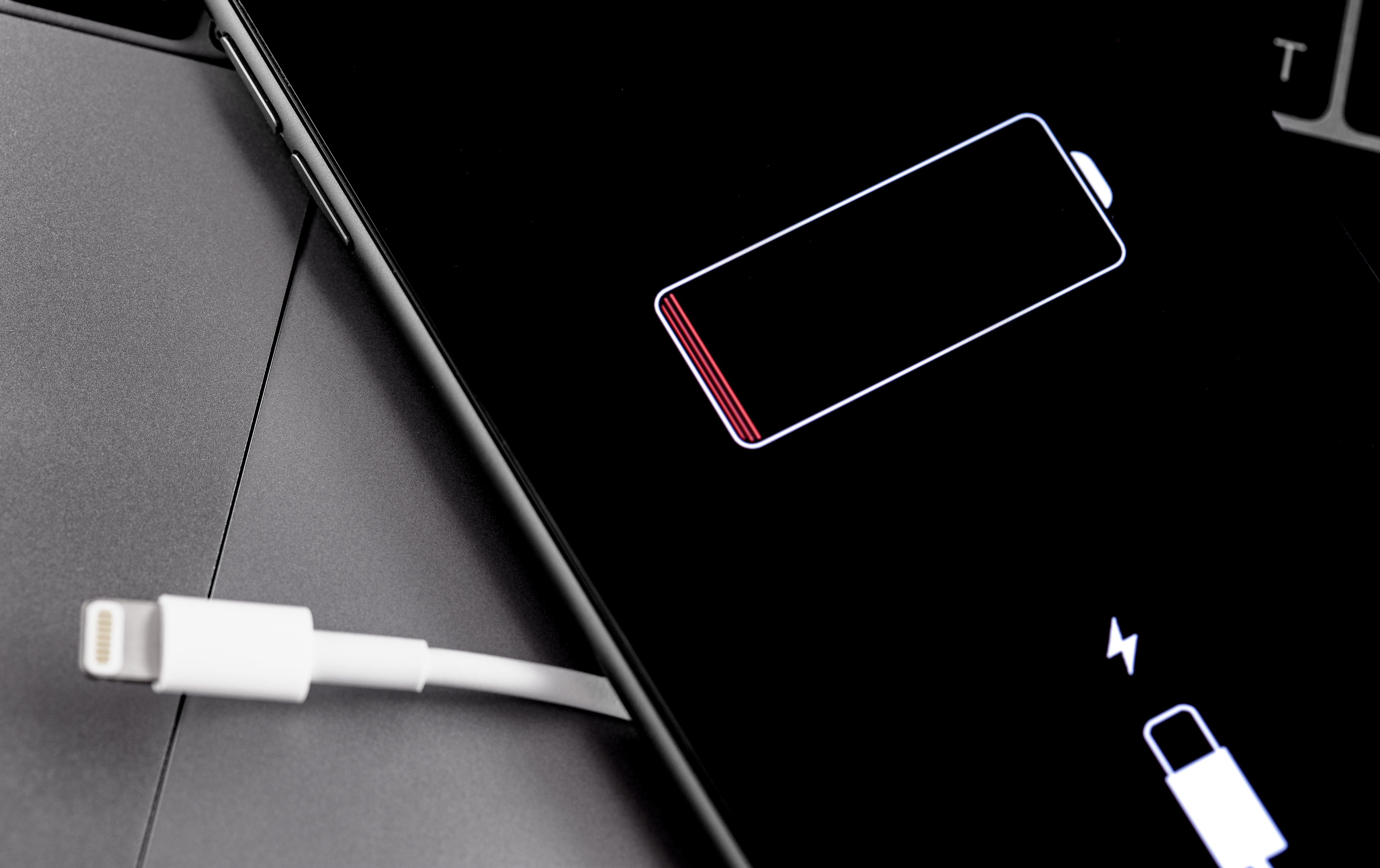 iPhone на серой поверхности со значком низкого заряда батареи и зарядным кабелем слева от телефона.