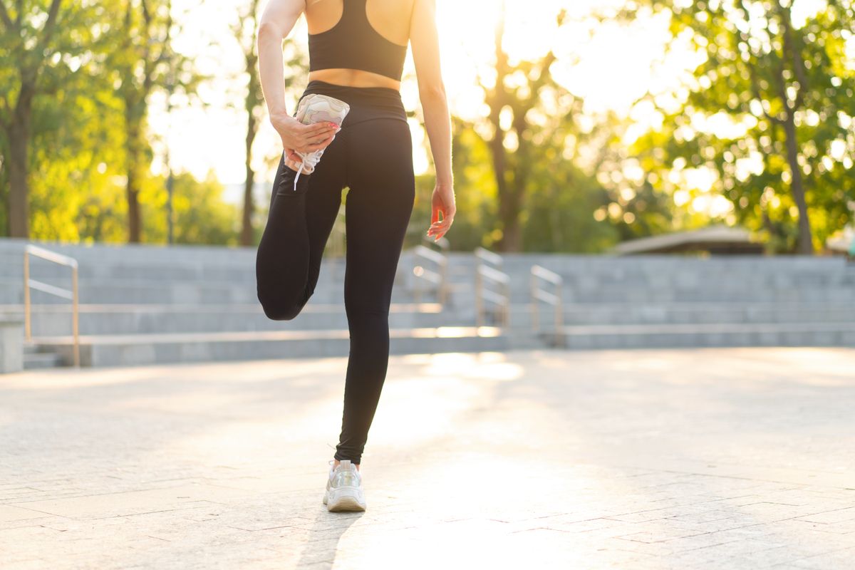 A woman warming up for a run outside. The photo show her from behind with her head cropped, and she&#039;s stretching her leg