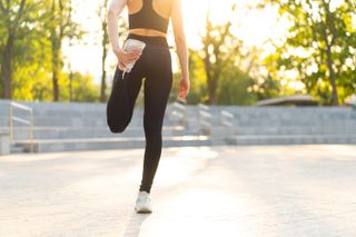 A woman warming up for a run outside. The photo show her from behind with her head cropped, and she's stretching her leg