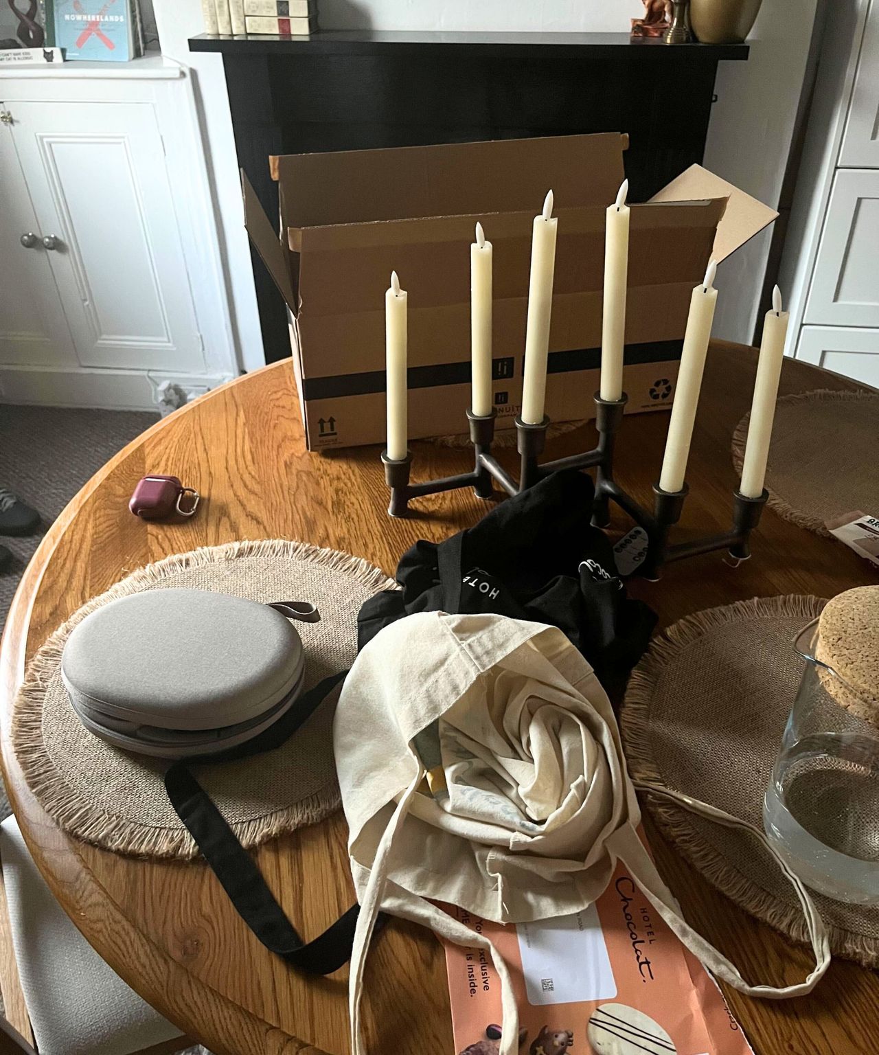 A round wooden dining table covered in bags, boxes, and mail.