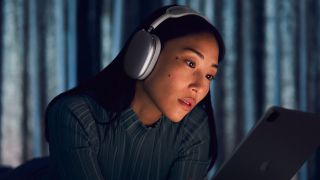 a woman staring at an ipad while wearing the apple airpods max wireless headphones