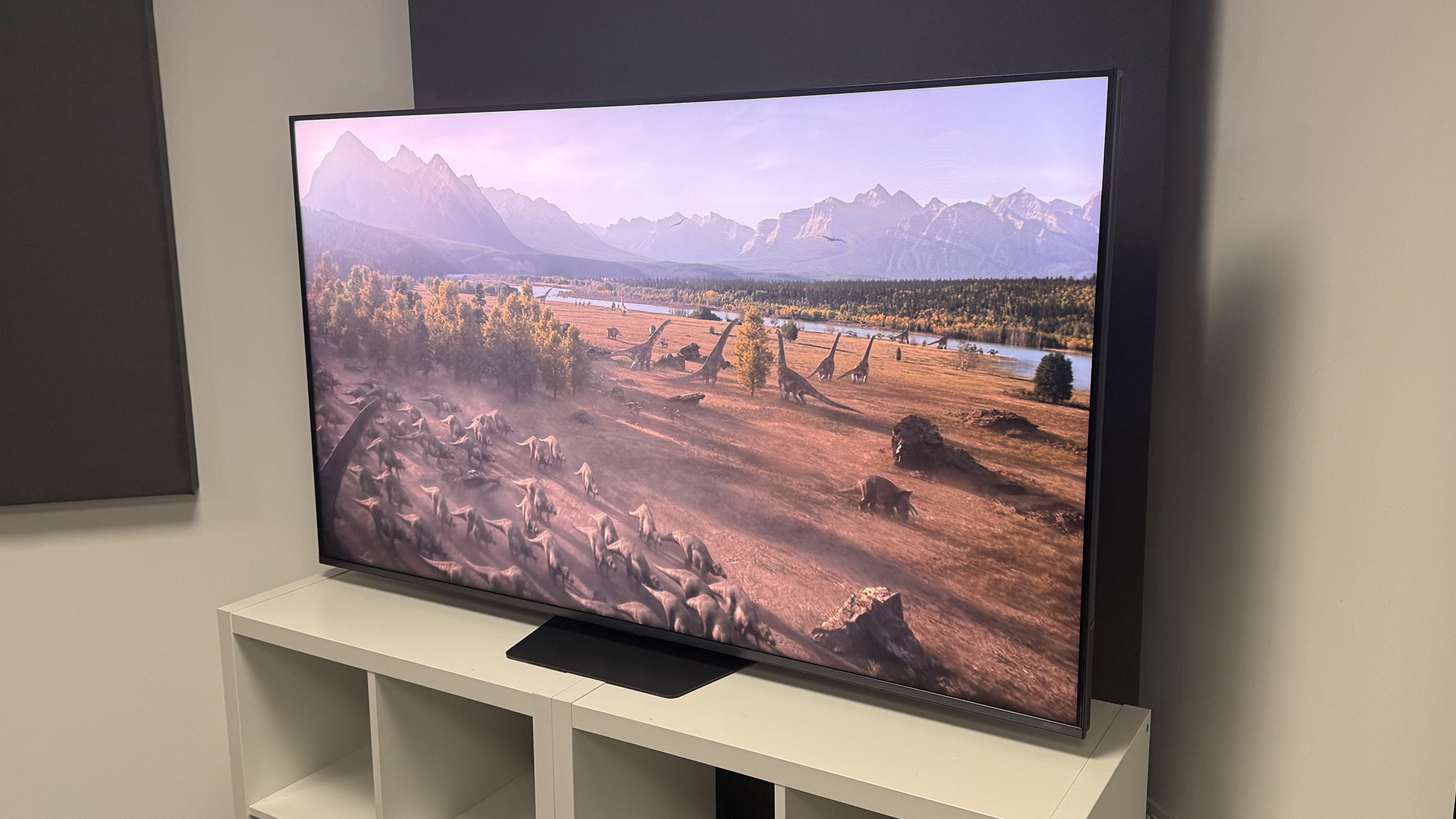 The 65-inch Hisense UR9 RGB Mini LED TV, photographed on a white, wooden unit. On the screen is a still from Netflix documentary, The Dinosaurs.
