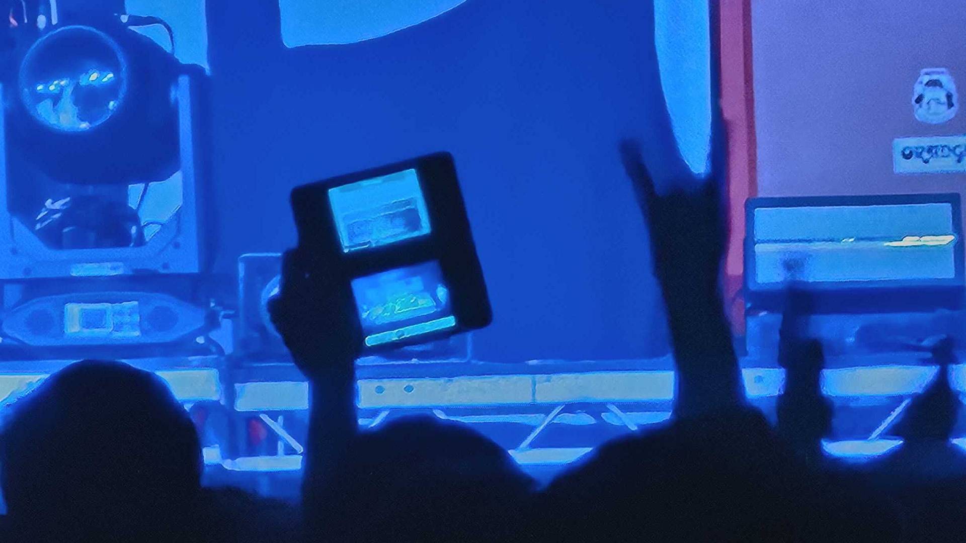 Zoomed in photo of someone holding DSi XL handheld in one hand while making devil horns with other hand.