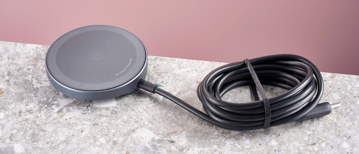 The top of the Anker Wireless Charging Pad, which is sitting on a grey stone-effect surface, against a light pink background. Its cable is neatly wound and secured with a thin black elastic band. 