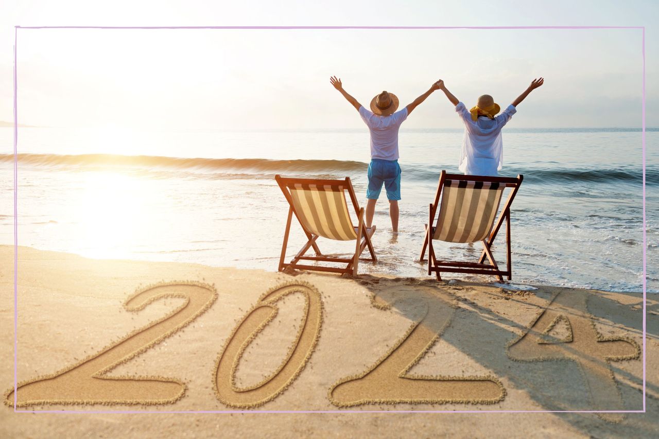 Couple on beach with deckchairs stood up 2024 written in sand