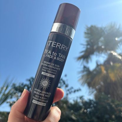 a hand holding a bottle of by terry tea to tan in the sunshine