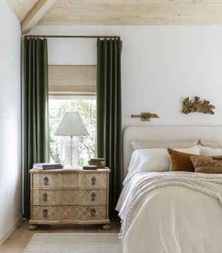 white bedroom with green curtains and wooden nightstand by Marie Flanigan