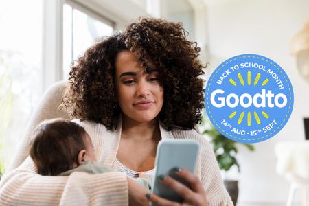 A woman smiles while looking at her phone and holding her sleeping baby