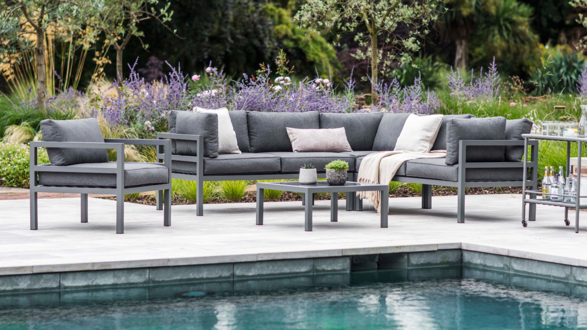 A grey metal outdoor sofa and armchair by the side of a swimming pool