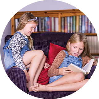 Image of two young girls sitting on a chair reading a book