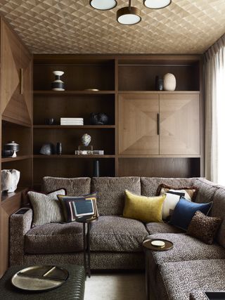 living room with wooden storage, textured ceiling, brown sofa, blue and yellow cushions, curtains, footstool