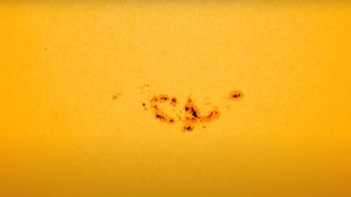 spacecraft view of a patch of the sun's yellow surface, showing a large, dark, irregular sunspot