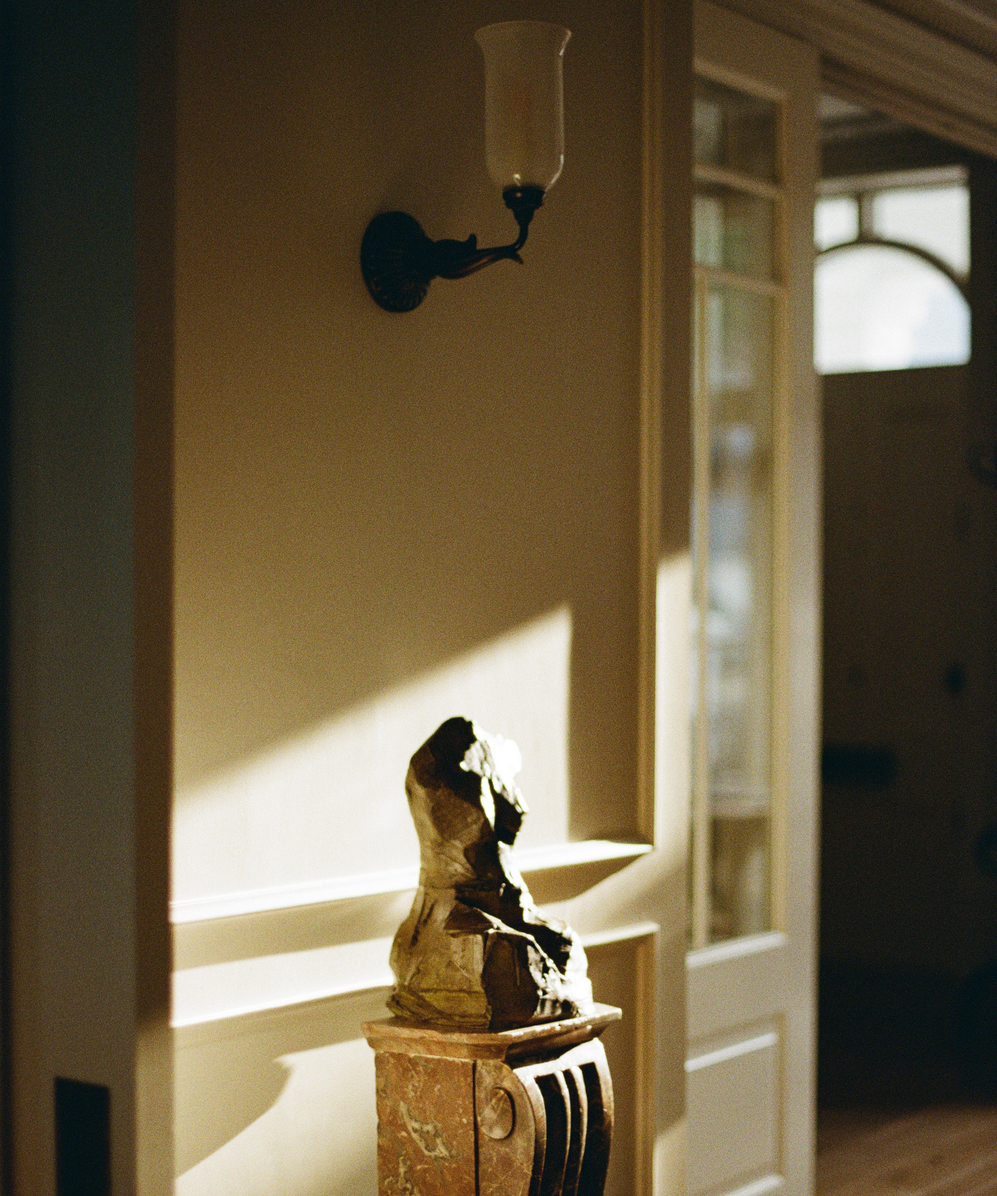 sculpture of a woman's body on a pedestal in a hallway with sunlight shining directly across it