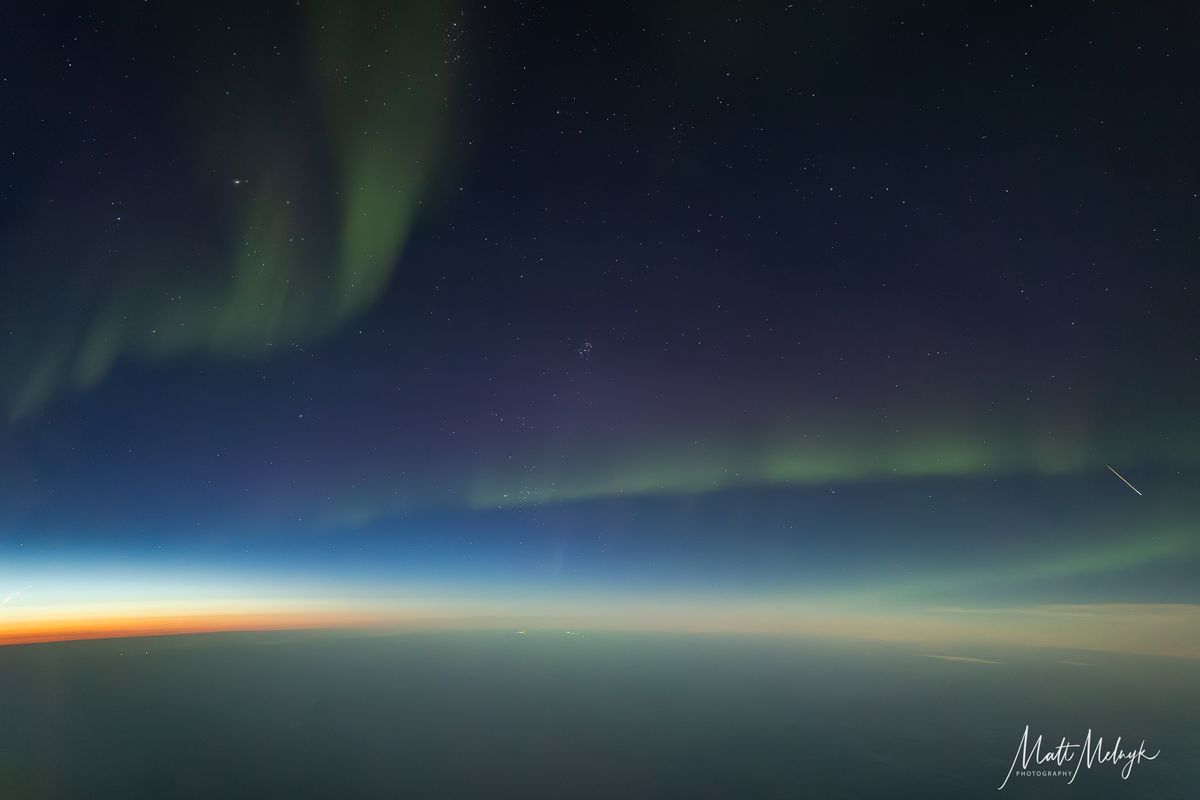 A lone meteor is pictured streaking through a sky wreathed in a twisting green aurora in a scene shot from an airplane. The curvature of Earth is visible below.