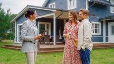 A female real estate agent shows a home to a young couple, exterior view.
