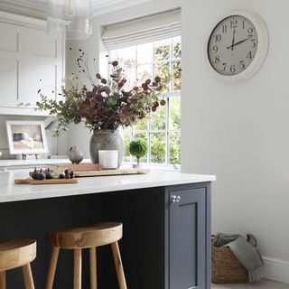 a neutral shaker-style kitchen with an island with a breakfast bar and a wall-hung clock