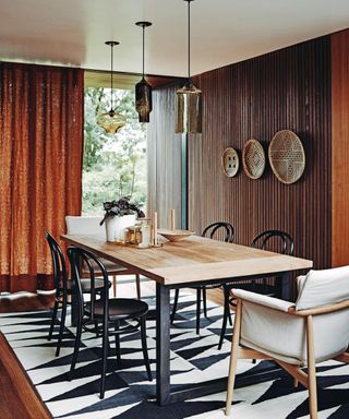 A dining room color idea with brown wooden clad walls and matching brown curtain over floor to ceiling window, with black and white furniture