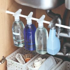 An under-sink storage space with a tension rod used to hang cleaning sprays