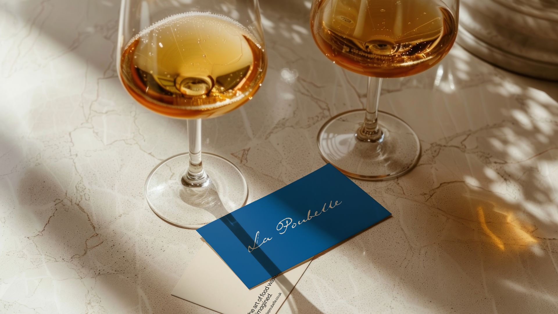 an image of two wine glasses with orange wine on a marble table with two business cards in front of them