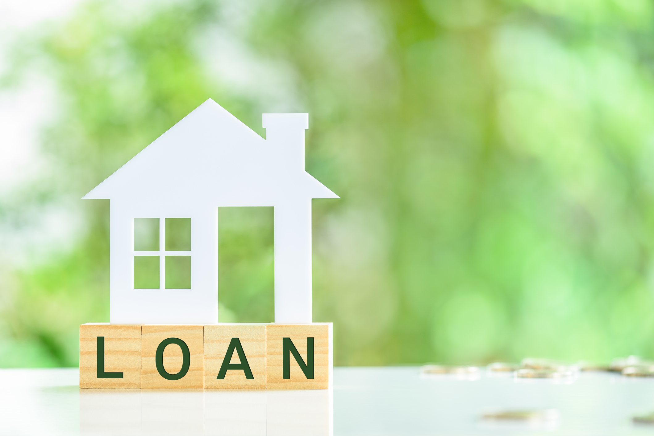 white cutout house on top of wood blocks that say "loan" with coins and trees in the background
