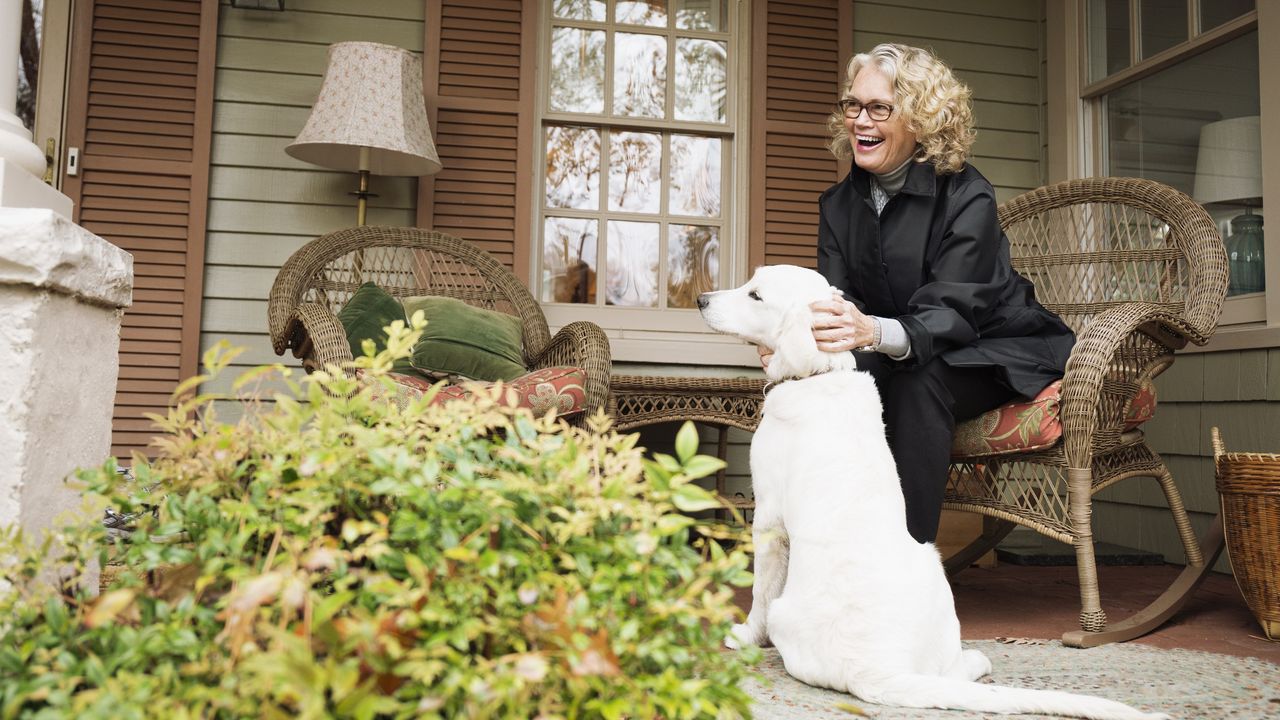 A smiling older woman and her dog hang out on her front porch.