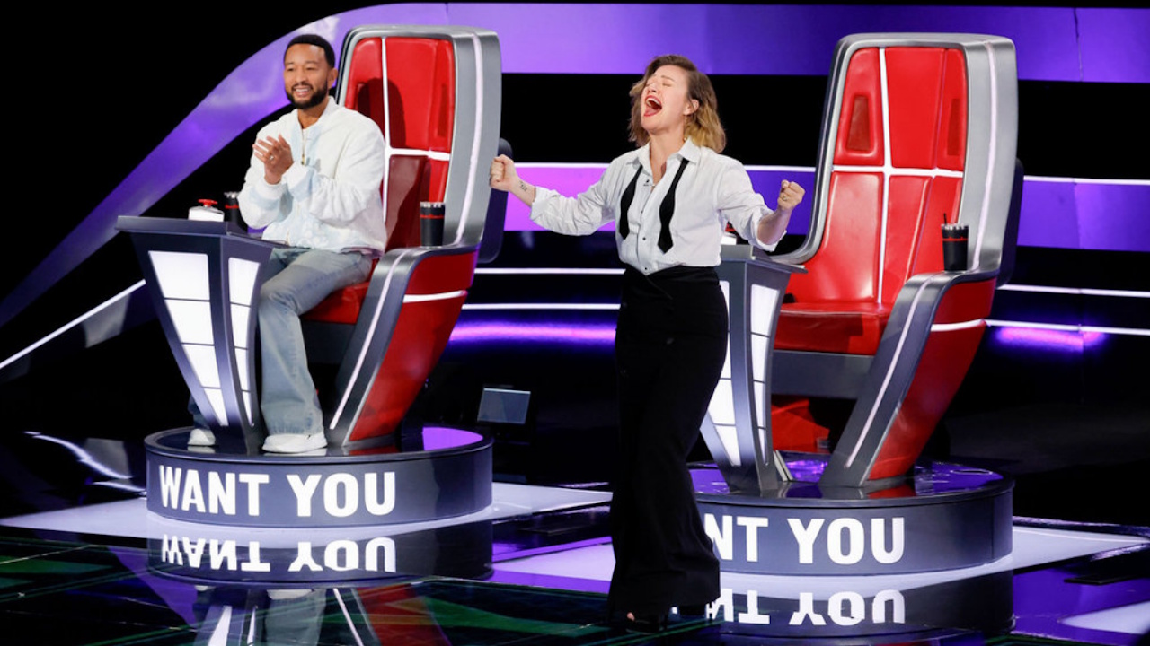 Kelly Clarkson screams in anguish on The Voice Season 29, as John Legend smiles behind her.