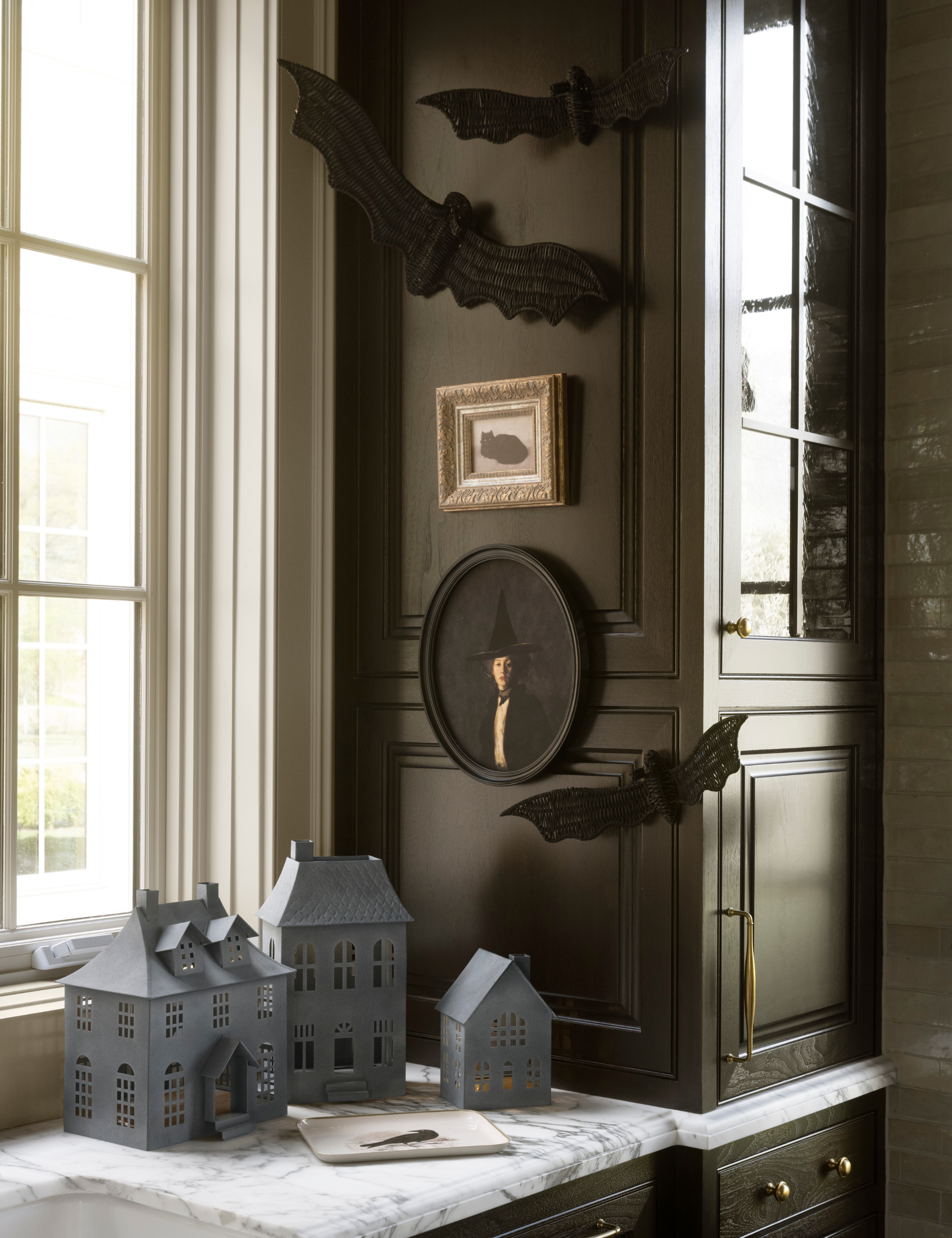 Halloween vignette by Shea McGee, featuring antique wall art, wicker bats, and iron haunted houses.
