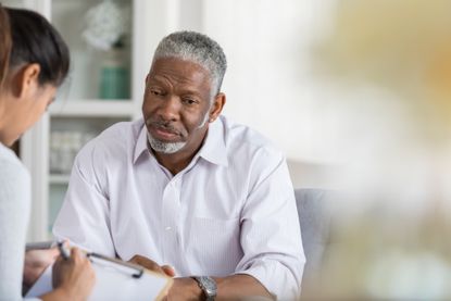 A man talks to a woman as she takes notes