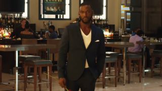 Kofi Siriboe stands in a lobby holding a rose in Girls Trip.