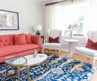 living room with coral sofa and two white chairs with blue rug