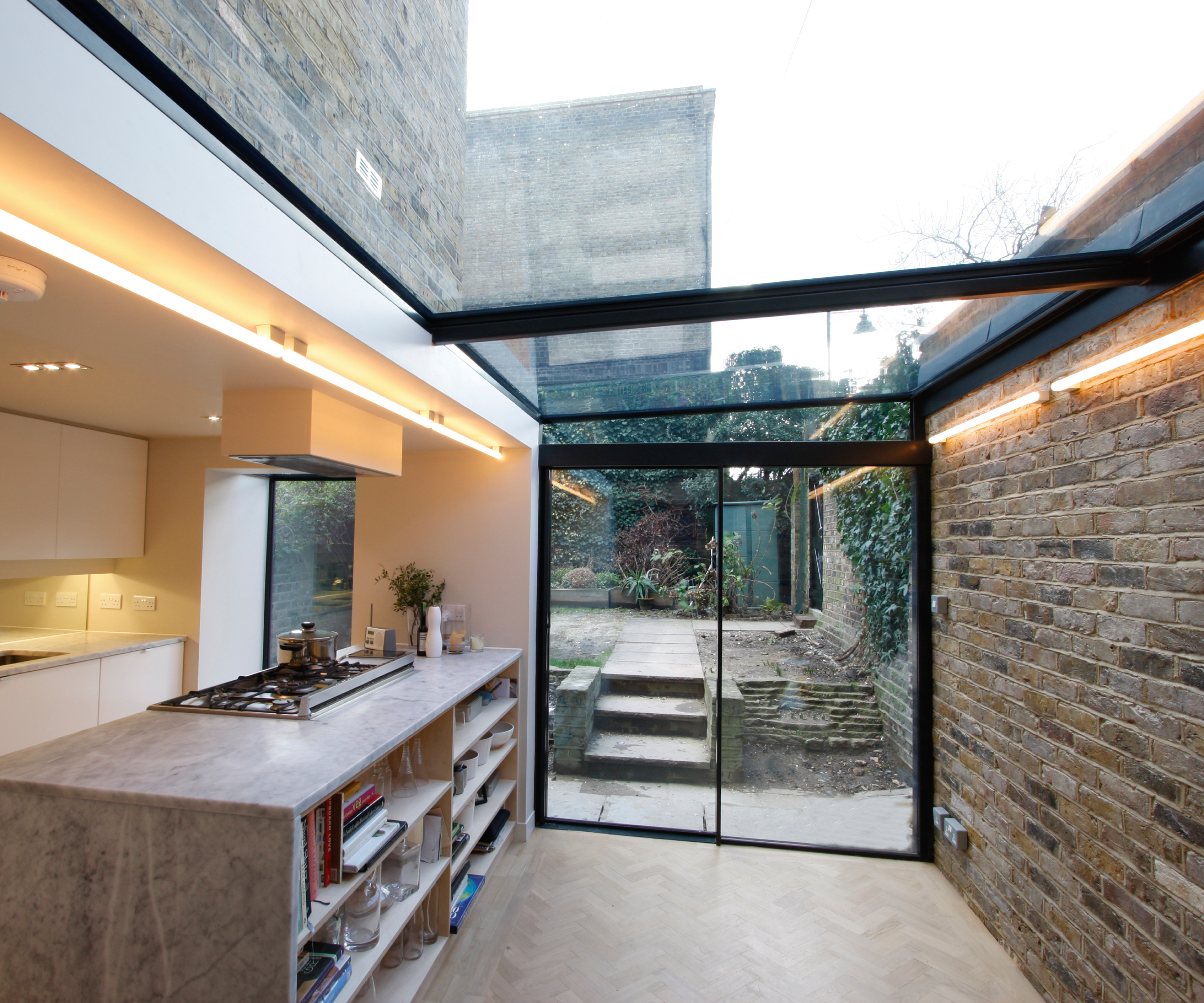kitchen extension with majority of roof in glass, one brick wall, sliding doors leading to outdoors and strip lighting highlighting roof and kitchen area