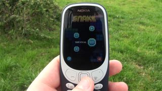 En person, der holder en Nokia 3310 med en græsplæne i baggrunden.