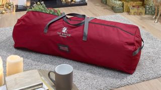 A burgundy tree storage bag with gray handles laying on a gray rug, for the best Christmas storage bags.