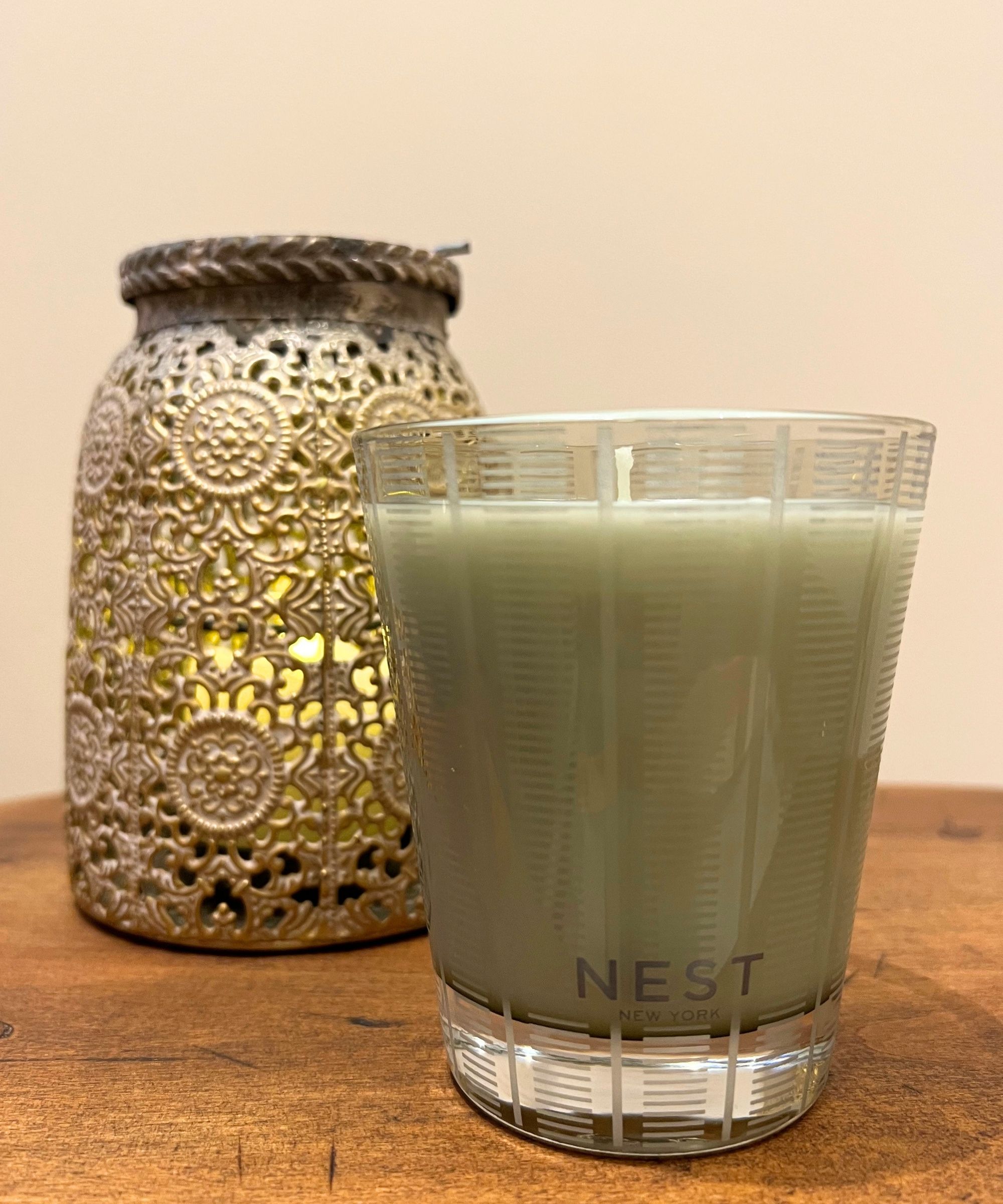 Nest mint and eucalyptus candle on a wooden stool with a gold lantern behind in front of a white wall