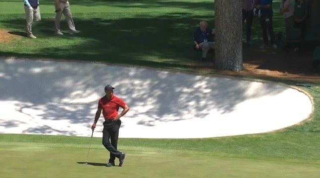 Tiger Woods on the 16th green at Augusta National with Verne Lundquist watching on in the distance