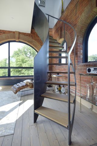 curved metal staircase in brick living room with windows