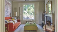 Traditional living room with orange sofa and marble fireplace with a green ottoman and a wall hanging
