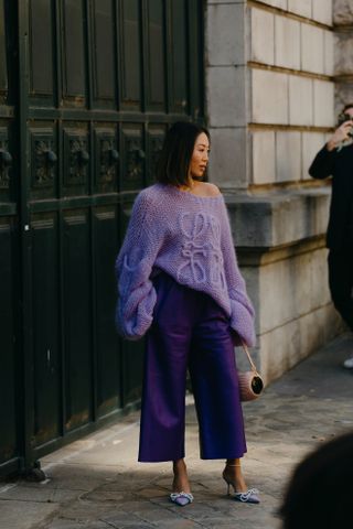 A woman at Paris Fashion Week wearing a purple open-knit Loewe sweater, purple pants, and purple bow heels