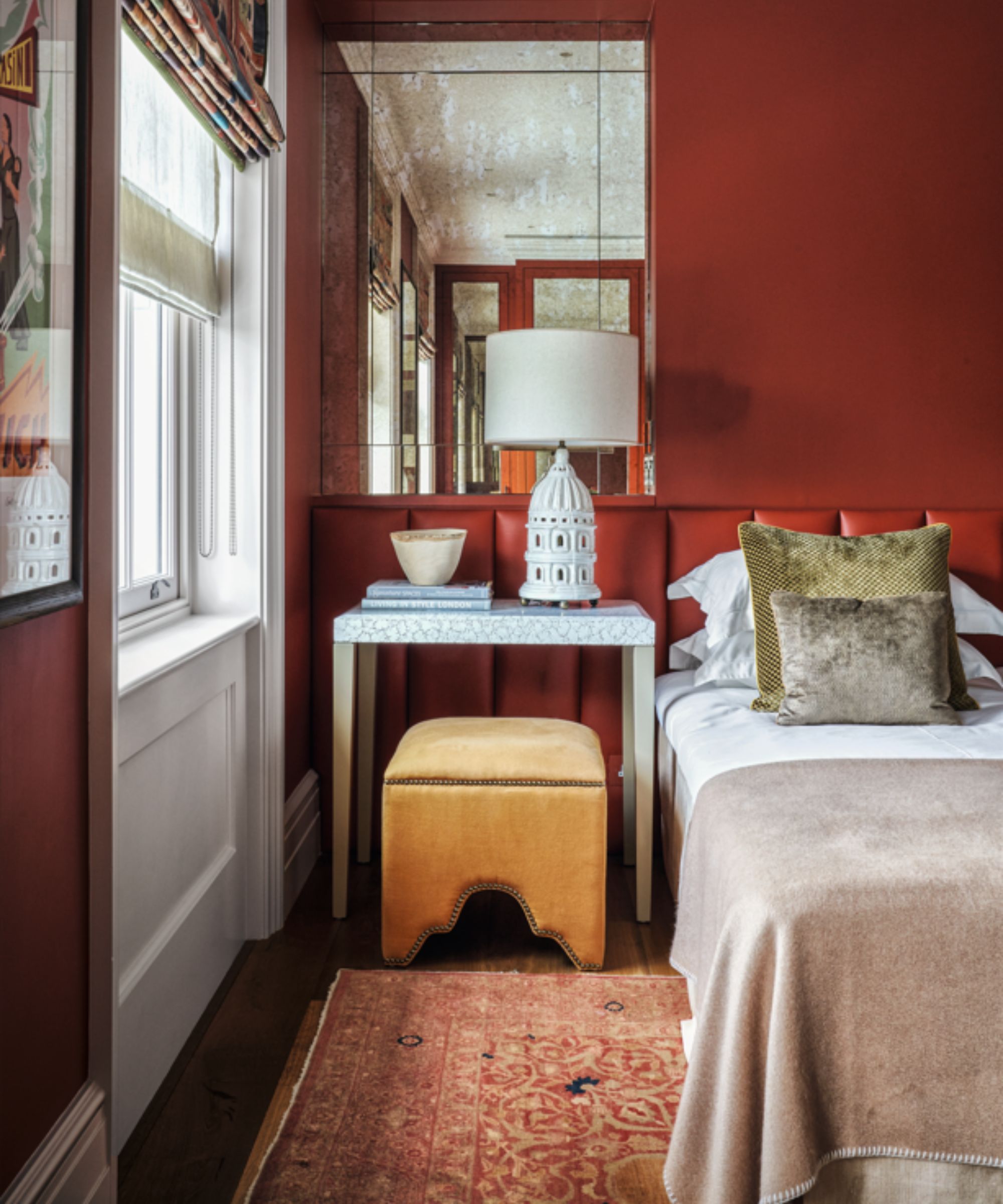 wall to wall upholstered headboard in a bedroom painted red with a small mustard yellow stool